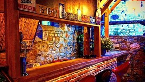 A bar area with a brick counter, two red bar stools, and a stone wall backdrop. - Eski Datça Evleri Mini Hotel (Datça)