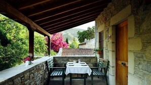 A stone building with a wooden door and a covered patio area with a table and benches. - Eski Datça Evleri Mini Hotel (Datça)