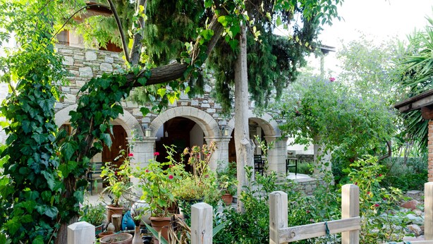A stone building with arched doorways, surrounded by lush greenery and potted plants. - Eski Datça Evleri Mini Hotel (Datça)