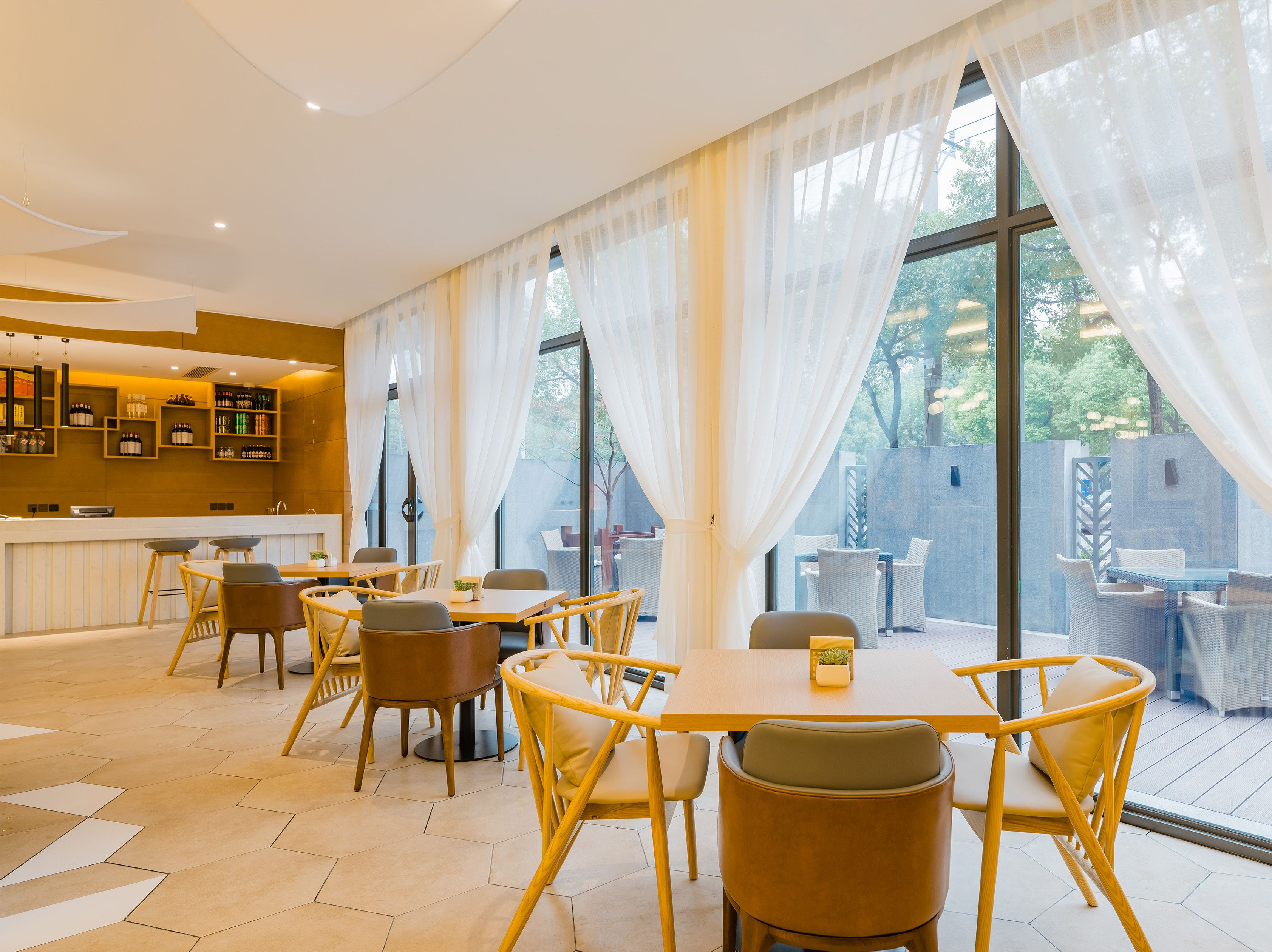 A modern dining area with hexagonal patterned flooring, round tables with chairs, and a bar area with shelves of bottles.