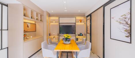 Un comedor moderno con una mesa de madera, sillas grises y un florero. Estantes con adornos decoran las paredes.
