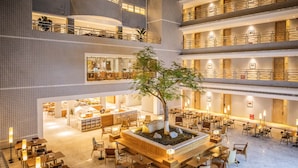A multi-level hotel lobby with a central seating area, multiple dining tables, and a large tree. - Atour Hotel Sun YatSen Mausoleum Scenic Spot Nanjing (Nanjing)