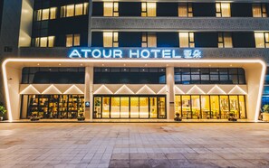 The exterior of Atour Hotel with a modern facade, large glass windows, and a prominent neon sign. - Atour Hotel Wujiang Suzhou (Suzhou)