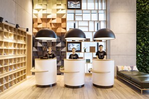 A reception area with three counters, a wooden shelving unit, and a bed with pillows. - Atour Hotel Wujiang Suzhou (Suzhou)