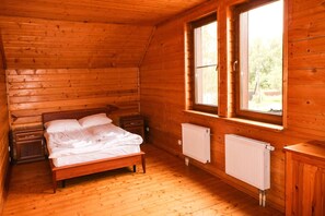 A wooden cabin bedroom with a bed, nightstands, a window, and a radiator.