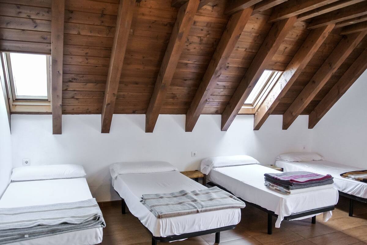 Un dormitorio con cuatro camas individuales, vigas de madera en el techo y un tragaluz.