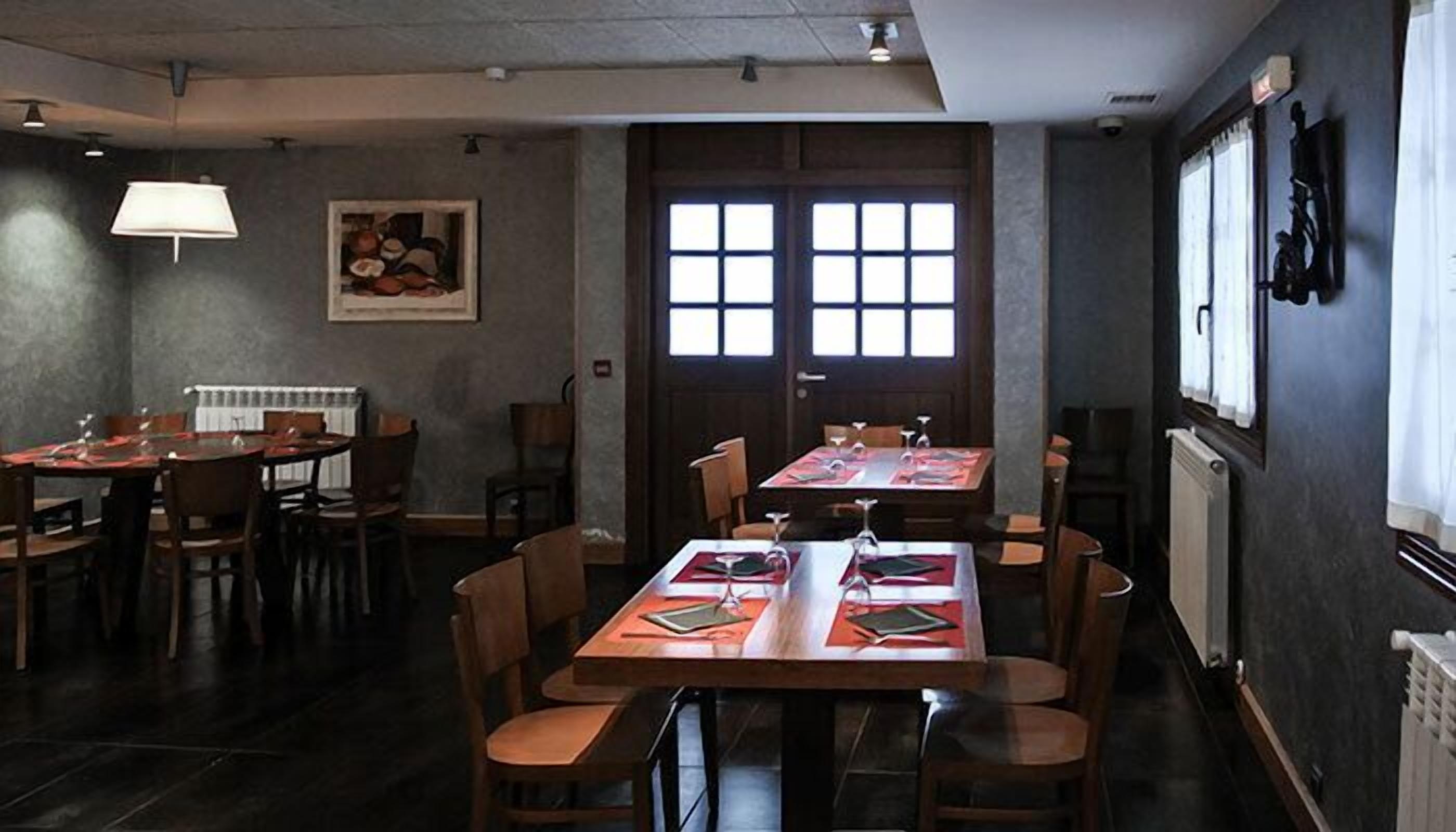 A restaurant with multiple tables and chairs, a large window with a view, and a framed picture on the wall.