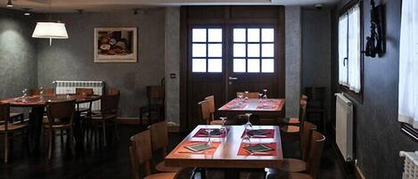 A restaurant with multiple tables and chairs, a large window with a view, and a framed picture on the wall.