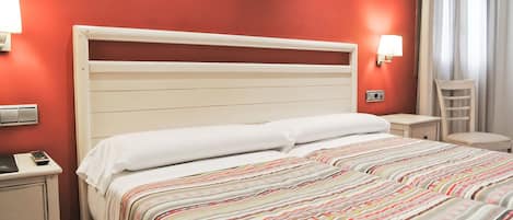 Habitación de hotel con cama, mesita de noche, una silla y una lámpara fijada a la pared.