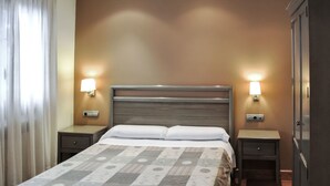 Una habitació d'hotel amb un llit, dues taules de nit, un armari i làmpades penjades a la paret.