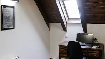 A room with a sloped ceiling, a desk with a computer, a chair, and a framed picture on the wall.