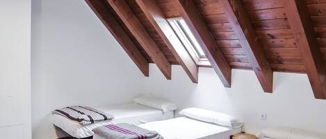A small, cozy room with two beds, wooden beams on the ceiling, and a skylight.