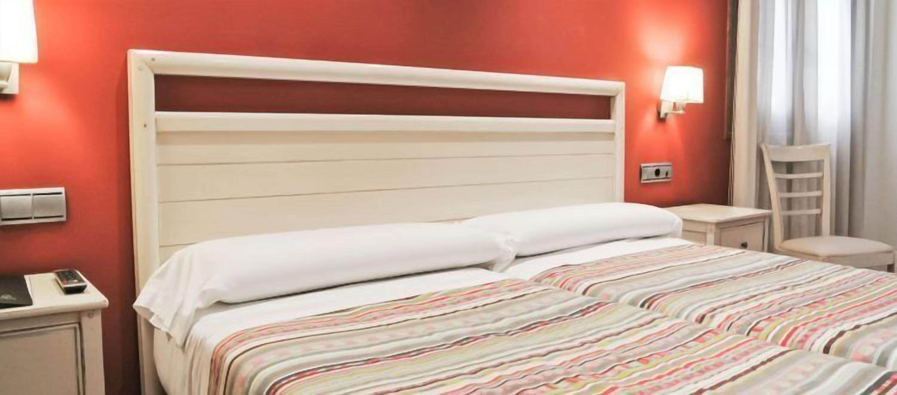 A hotel room with a bed, a nightstand, a lamp, and a chair.