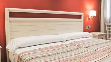 A hotel room with a bed, a nightstand, a lamp, and a chair.