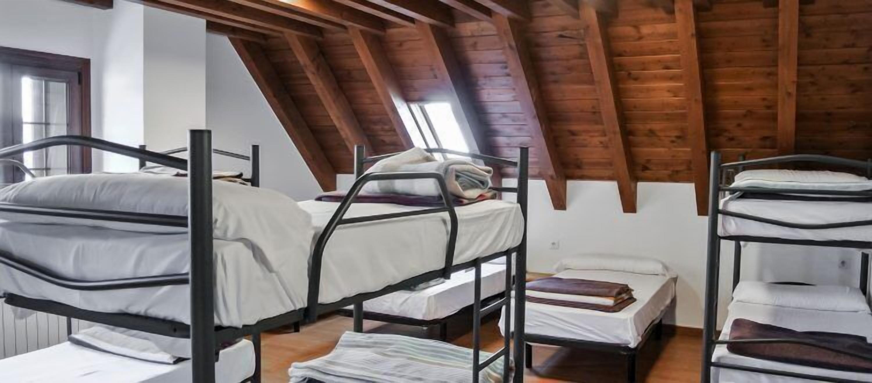 Un dormitorio con literas, vigas de madera en el techo y una ventana que deja entrar luz natural.
