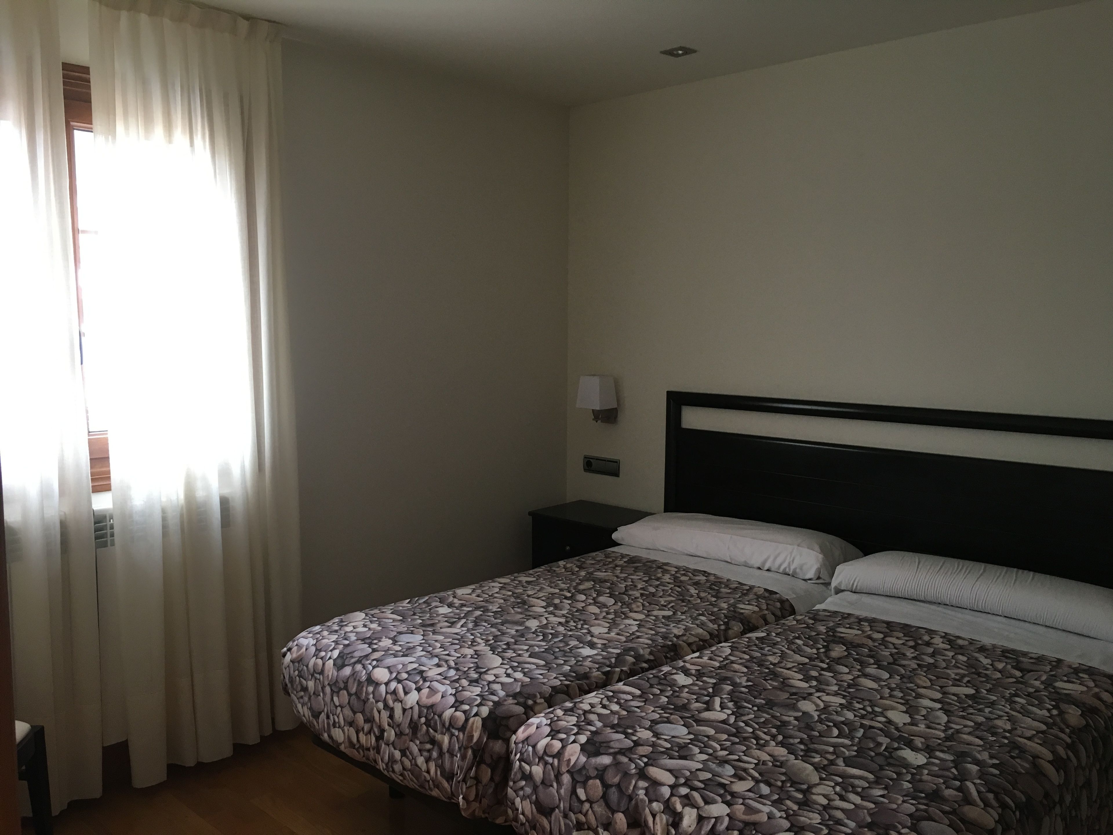 Een hotelkamer met een bed, gordijnen, een nachtkastje en een wandlamp.