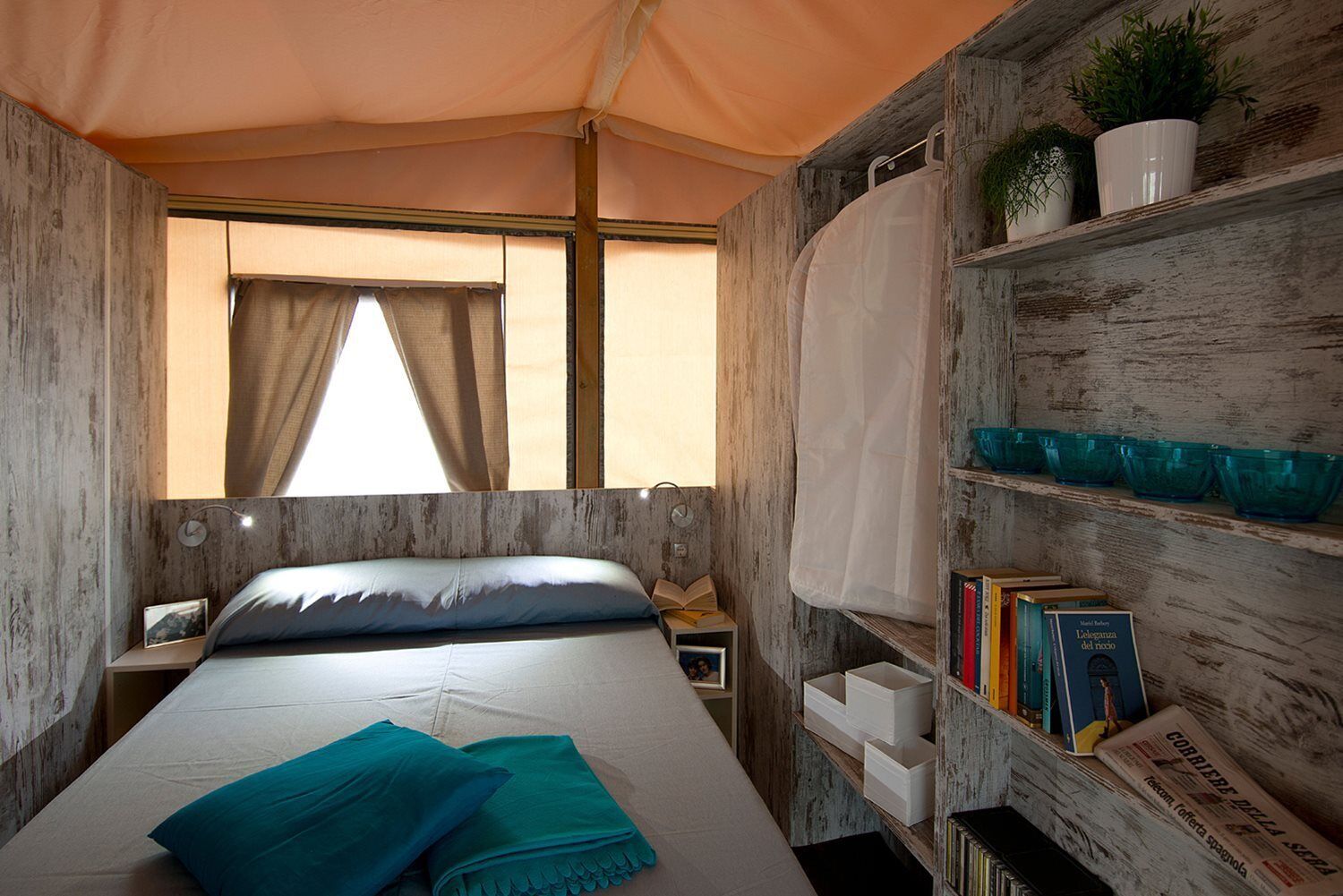 Ein gemütliches Zimmer mit einem Bett, einer Bücherwand und einem Fenster mit Vorhängen.