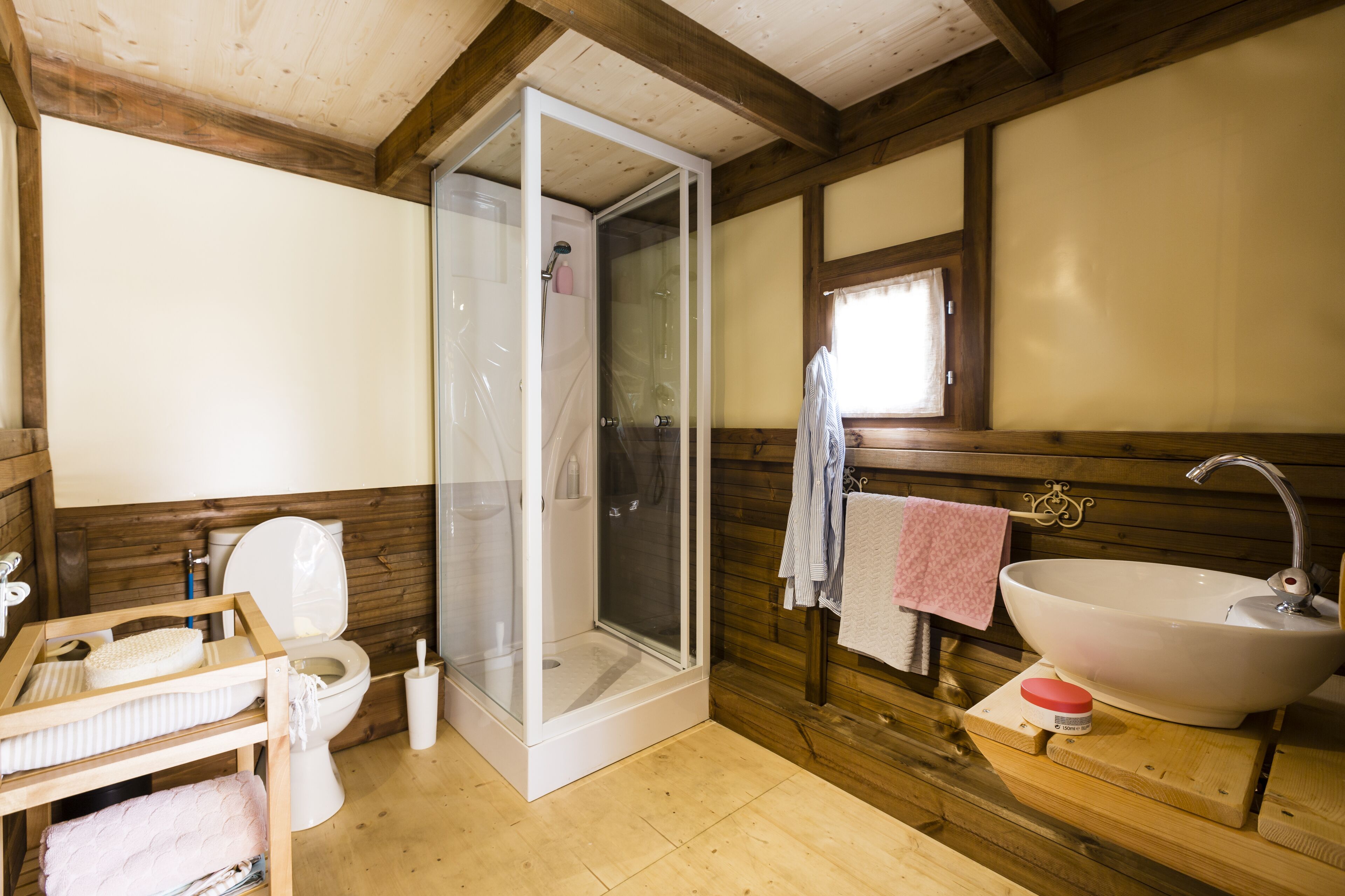 Een badkamer met een douche, toilet, wastafel en houten wanden.