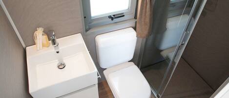 A compact bathroom with a white sink, toilet, and shower area.
