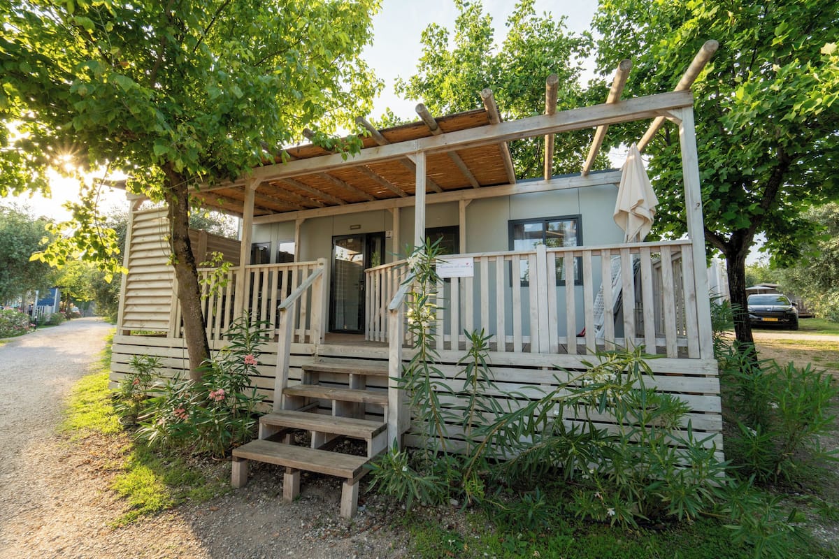 A wooden cabin with a porch, steps leading to the entrance, and a covered area with a bench.