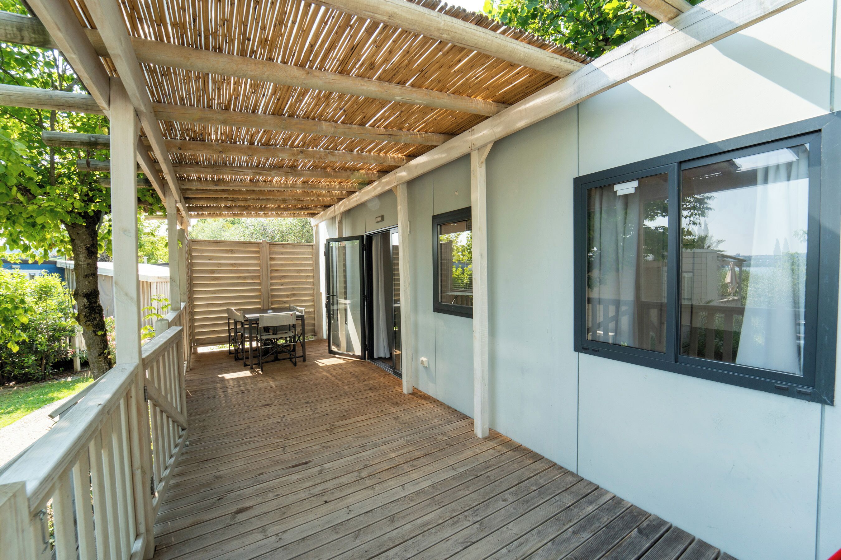 A covered patio with a wooden deck, a table and chairs, and a sliding glass door leading to a room.