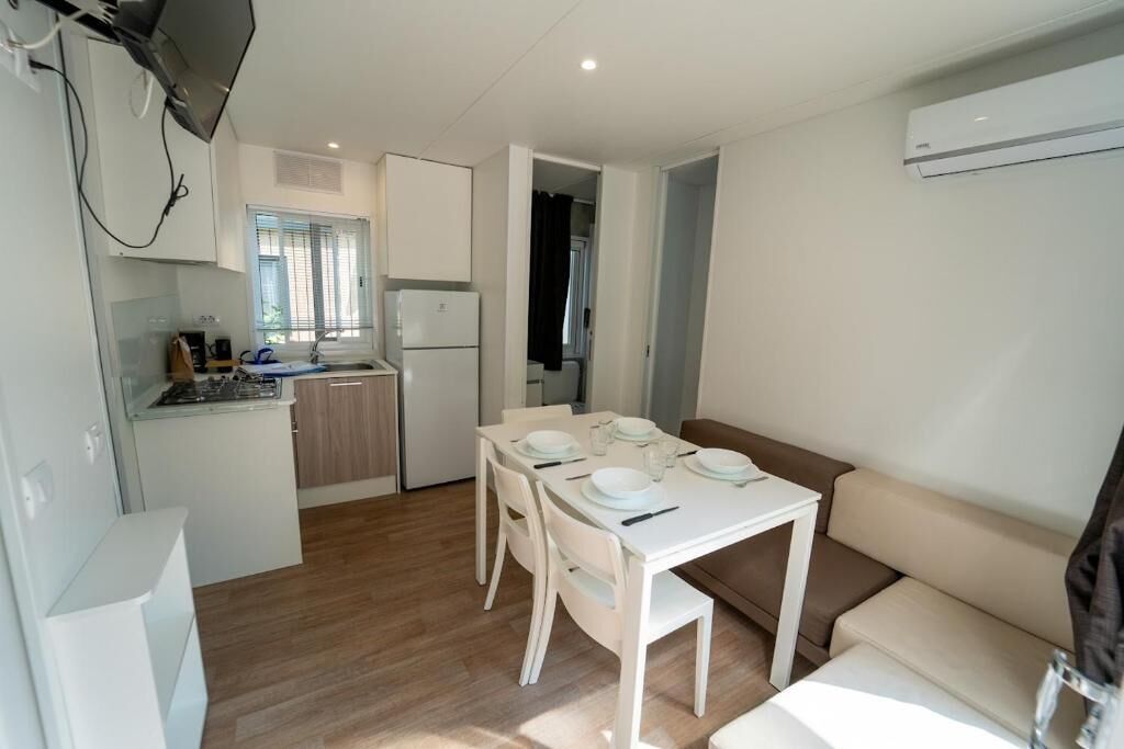 A compact kitchen with white cabinets, a dining table set for four, and a sofa in the living area.