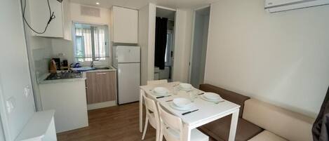 A compact kitchen with white cabinets, a dining table set for four, and a sofa in the living area.