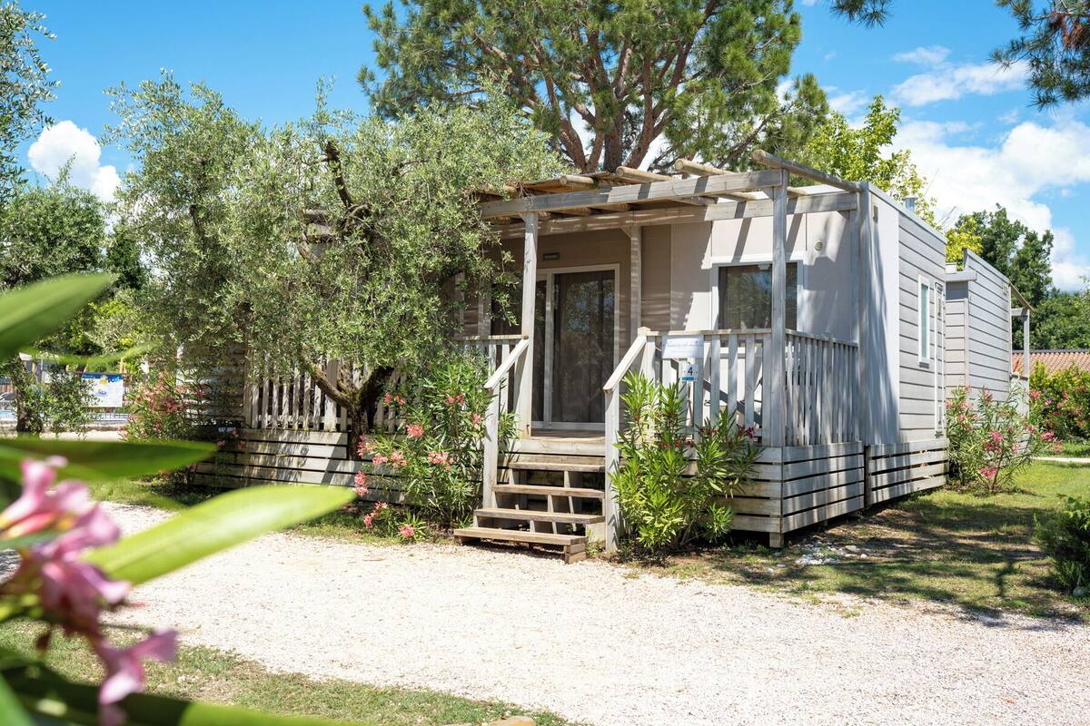 A small, single-story mobile home with a porch and a gravel driveway.