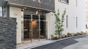 Een modern gebouw met een stenen gevel, een grote glazen ingang en een kleine boom op de voorgrond.