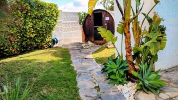 A stone pathway leading to a wooden door, surrounded by lush greenery and a well-maintained lawn.
