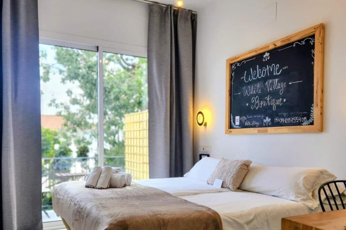 A bedroom with a bed, a wooden desk, a chalkboard sign, and a view of the outdoors.