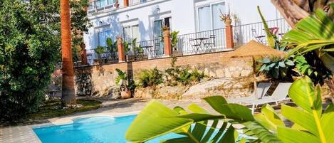 Una piscina rodeada de vegetación exuberante, con un edificio blanco que tiene balcones al fondo.