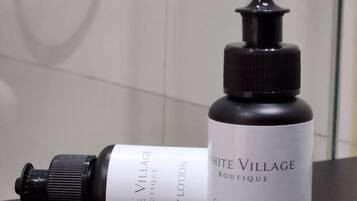 A bottle of White Village Boutique body lotion and a shower gel bottle on a black surface.
