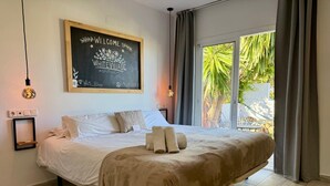 A bedroom with a bed, a welcome sign, a bedside table, and a window with curtains. - White Village Boutique, Benalmádena - Self Check-in (Benalmádena)
