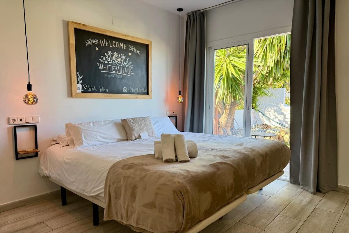 A bedroom with a bed, a welcome sign, a bedside table, and a window with curtains.