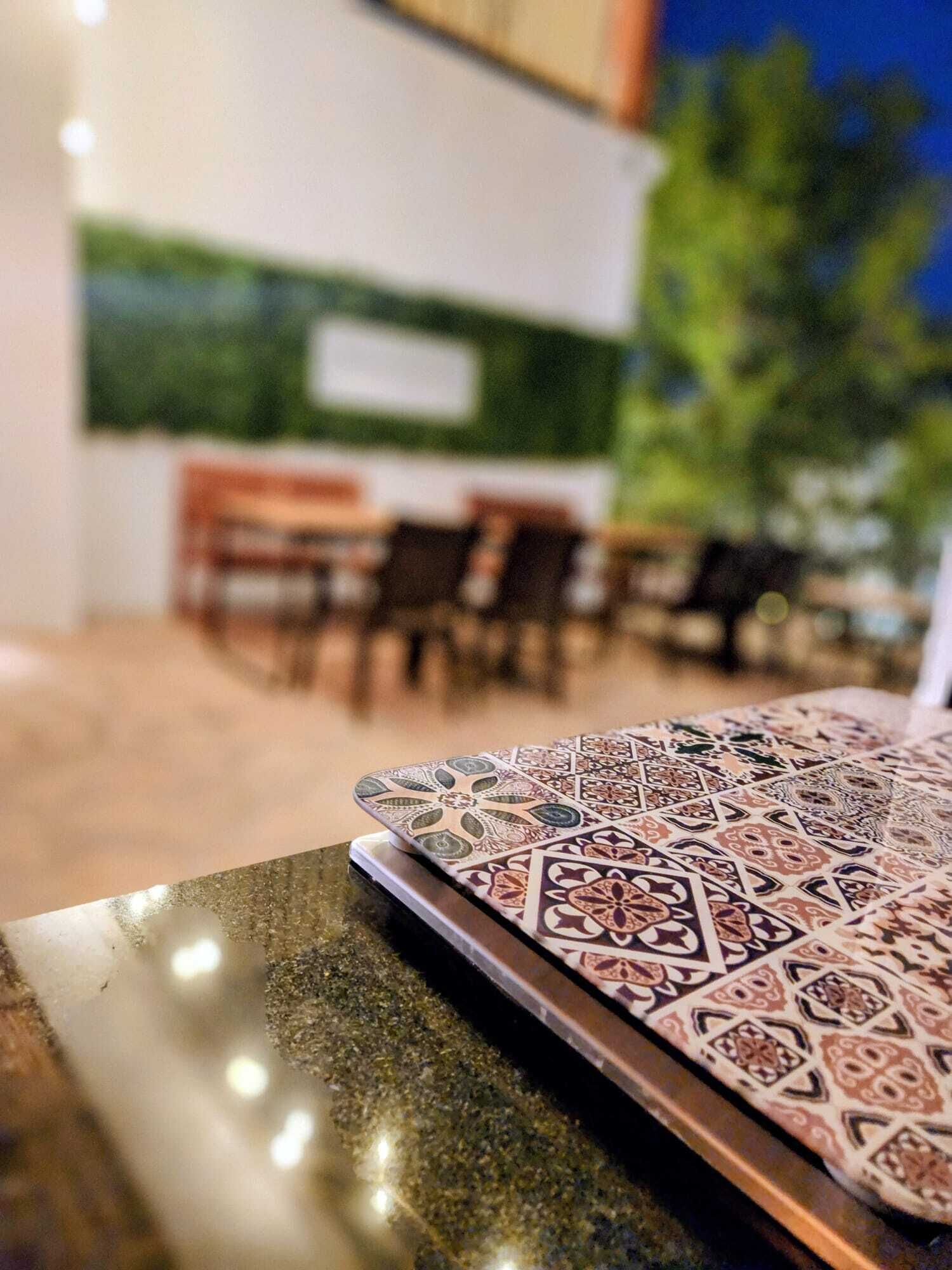 A dining area with tables and chairs, a patterned tablecloth, and a green wall in the background.