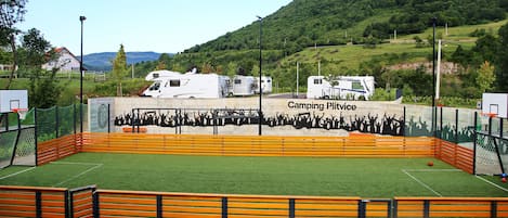 A sports field with a basketball hoop, surrounded by orange fencing, and RVs in the background.