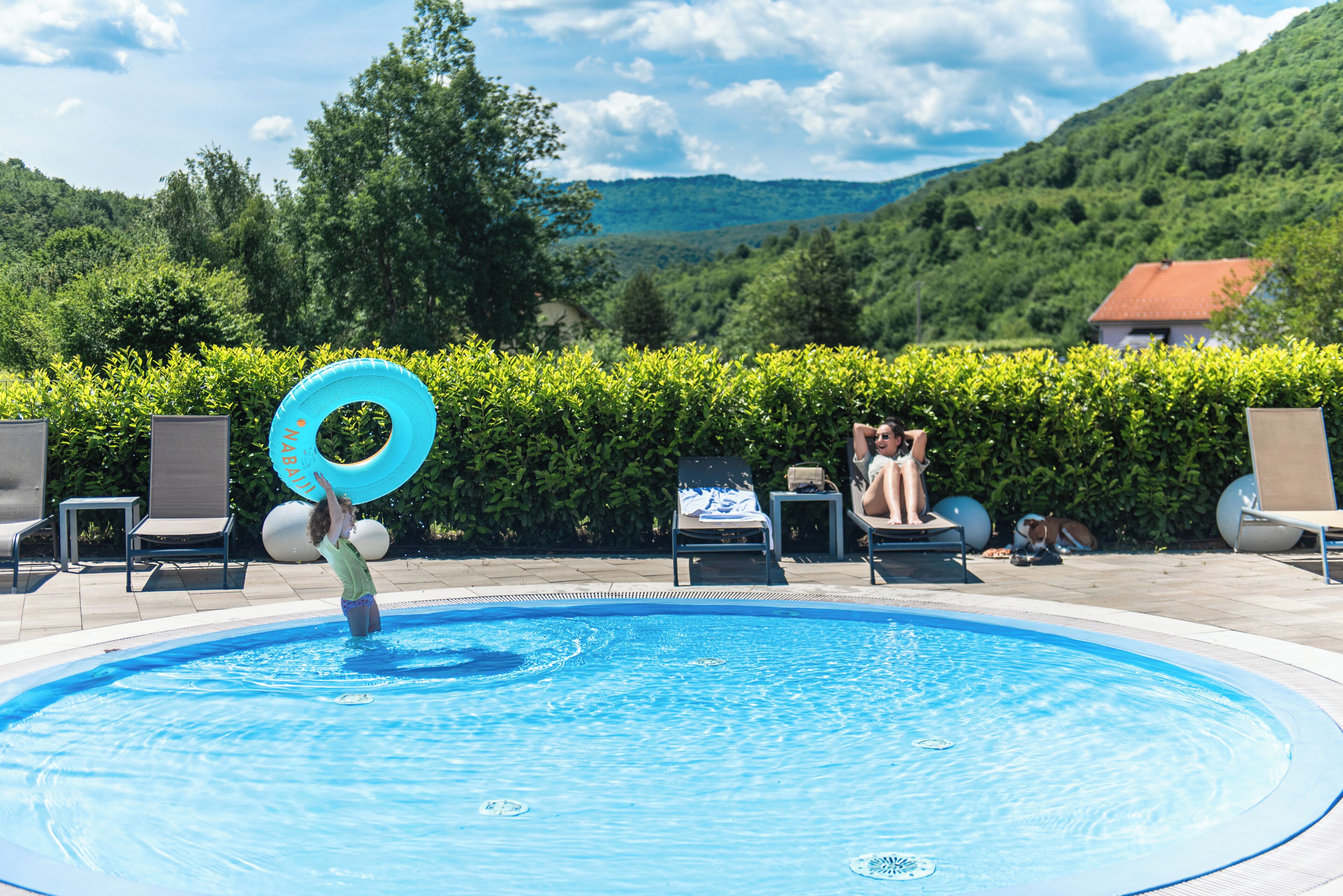 A swimming pool with lounge chairs and a person playing with a blue ring.