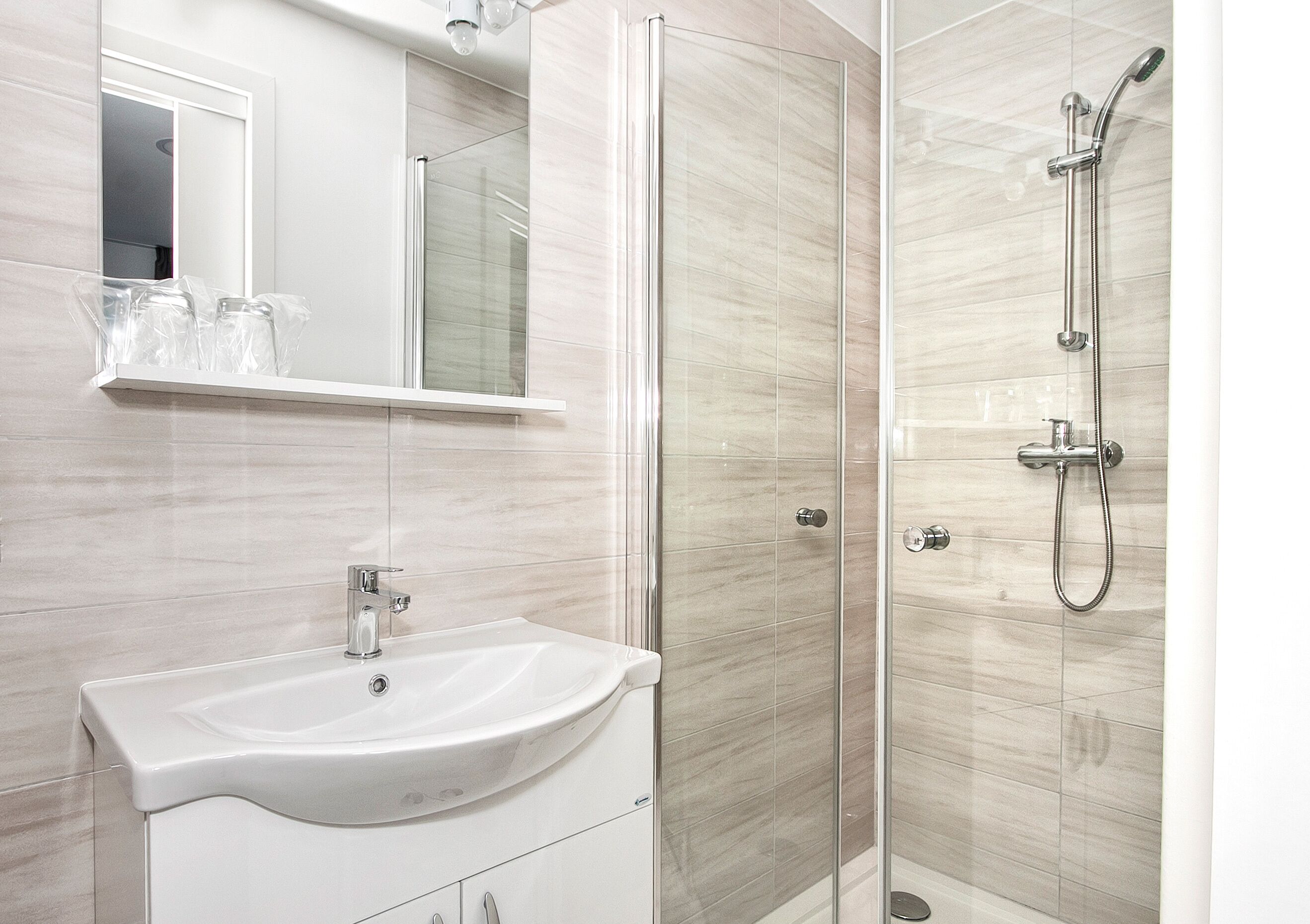 A modern bathroom with a glass-enclosed shower, a white sink, and a mirror above it.