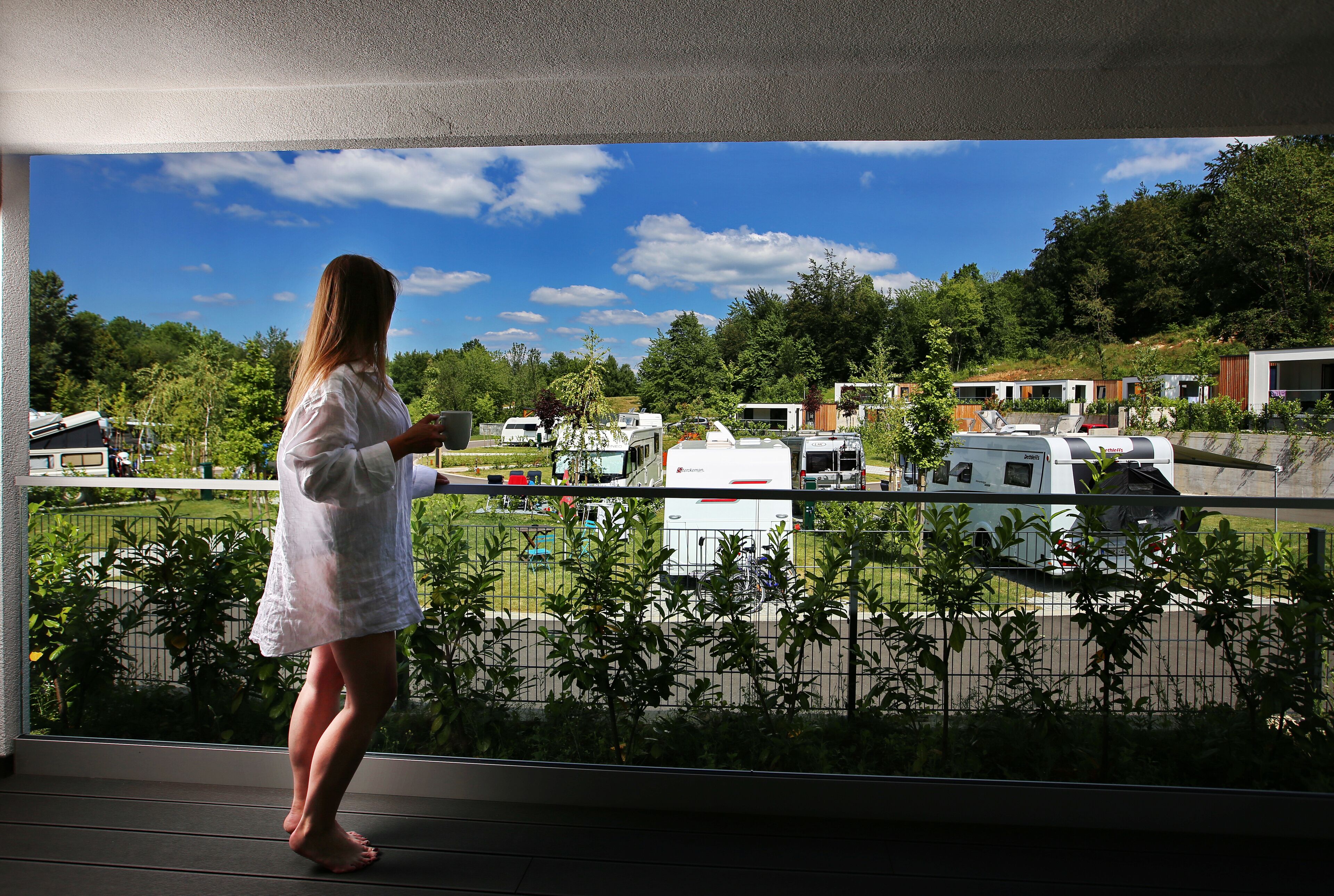 A person standing on a balcony overlooking a campground with RVs and mobile homes.