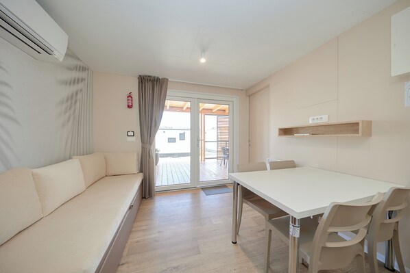 Una habitación moderna y minimalista con sofá, una mesa de comedor y sillas. Hay un ventanal corredero que da a un área exterior.