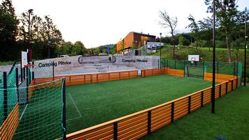 A sports court with artificial turf, surrounded by wooden benches and a netted fence.