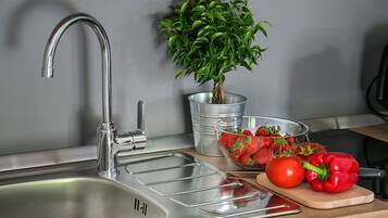 A kitchen sink with a modern faucet, a potted plant, a bowl of strawberries, a tomato, and a red bell pepper on a wooden cutting board.