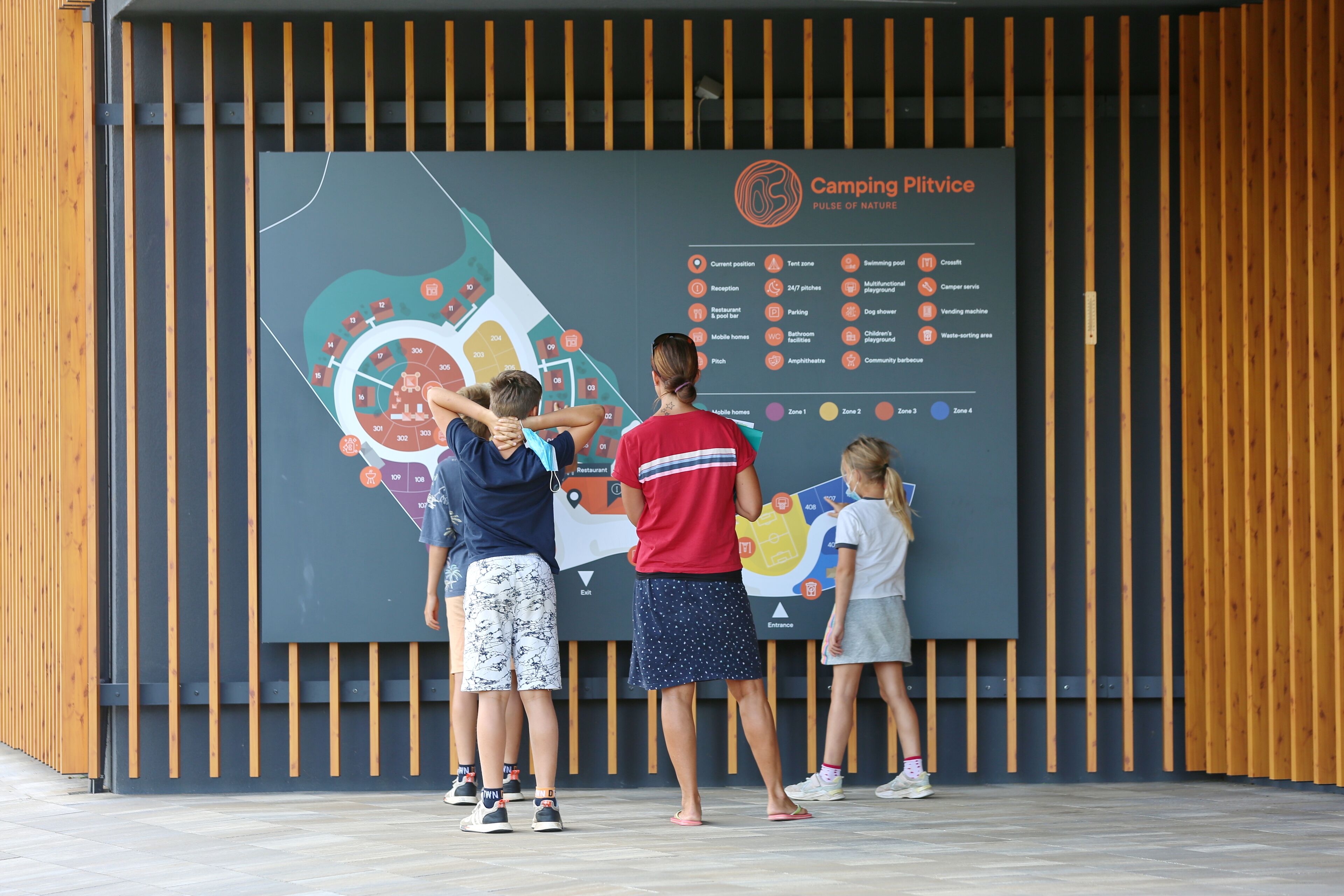 A group of people looking at a large informational display with various icons and text, likely detailing the amenities and layout of a camping facility.
