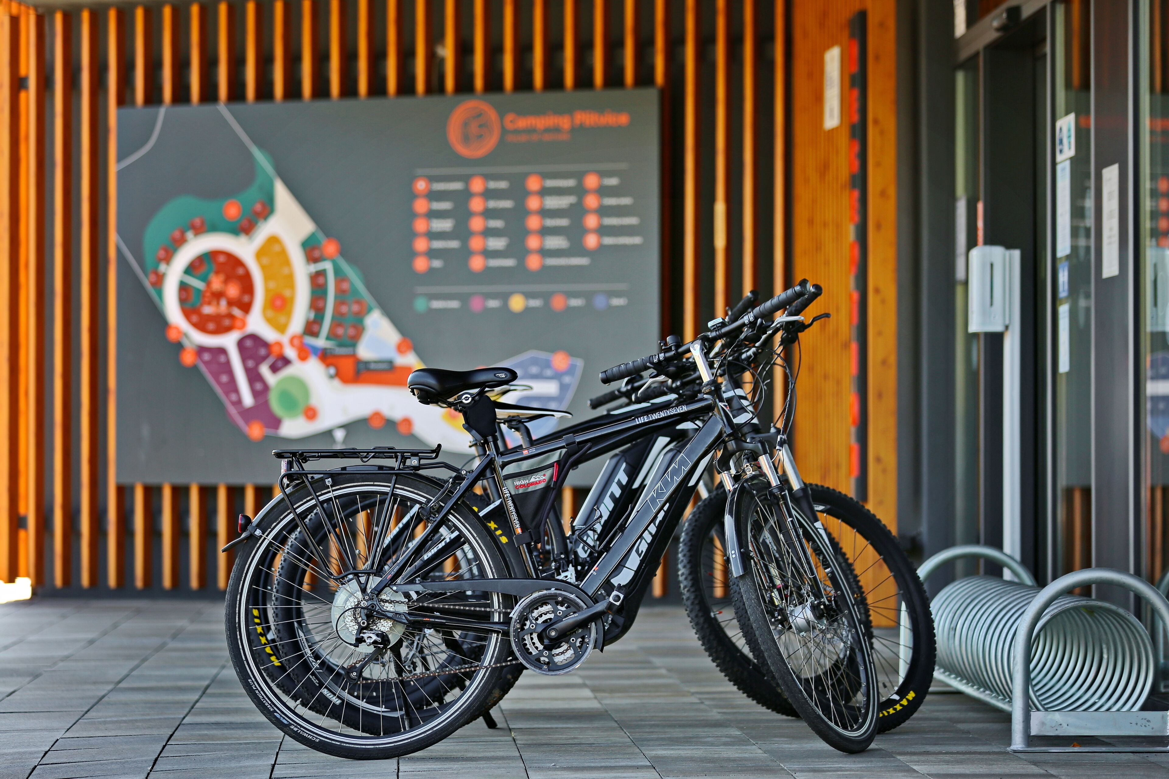 A black bicycle parked in front of a building with a colorful map and a list of amenities on the wall.