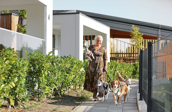 A woman walking two dogs on a paved path with greenery on either side.