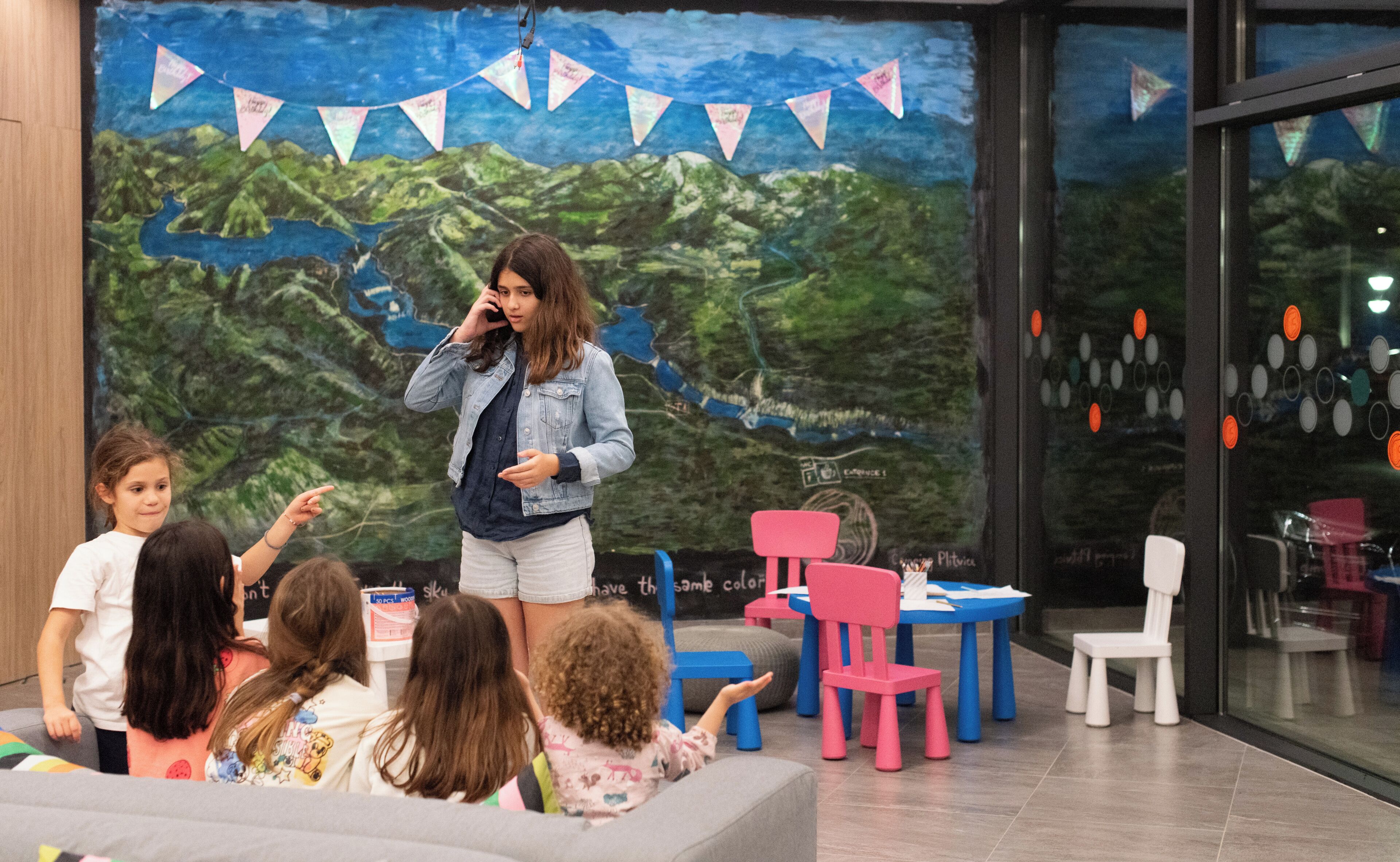 Une pièce décorée d’une fresque murale, avec des chaises et des tables pour enfants.