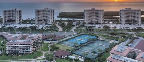 Un hotel de gran altura con varios pisos, una cancha de tenis y un puerto deportivo con barcos.