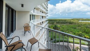 Un balcón con sillas de mimbre, vista al océano y barandilla blanca.