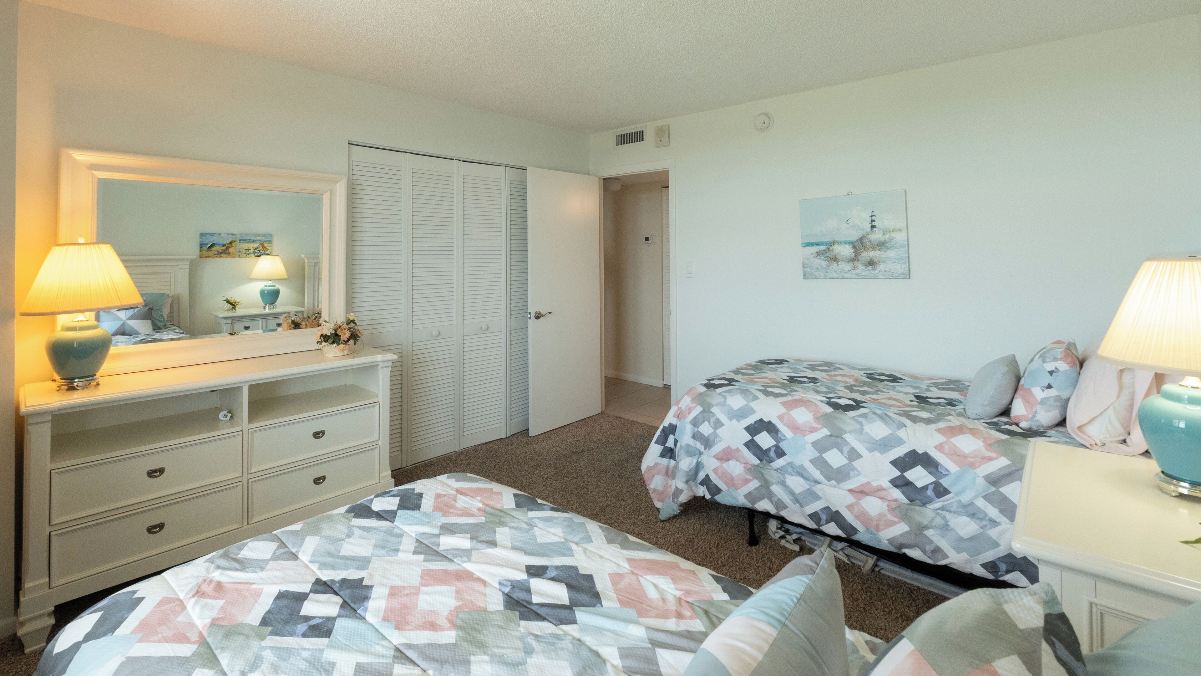 A bedroom with two beds, a dresser, a mirror, and a painting on the wall.